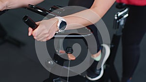 Close-up athletic woman spinning exercising workout on stationary cycling machine bike, indoors