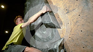 CLOSE UP: Athletic young man grabs a black volume hold while climbing indoors.