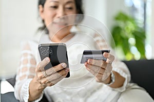 Close-up, An attractive Asian retire woman using her smartphone and holding a credit card