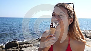 Close-up of attractive bikini woman eating an ice cream cone italian gelato turns around to the camera on the beach on summer
