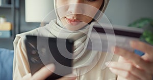 Close-up Attractive cheerful young Asian islam muslim beauty girl in hijab with casual sitting on couch use phone enjoy successful