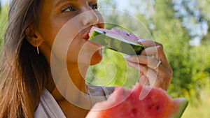 Close-up of an attractive cute young woman with kind eyes eating a piece of watermelon and smiling at the camera. A