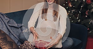 Close up of attractive girl wearing sweater and Christmas hat sitting on the sofa near Christmas tree finalize big