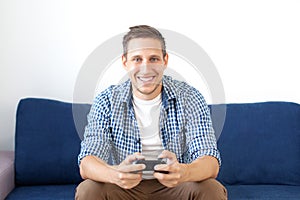 Close-up of an attractive guy with stubble in a shirt, holding a joystick and playing video games on TV on vacation, sits at home