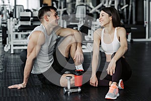 Close up of attractive pretty young fitness couple sitting together and having a break in the gym