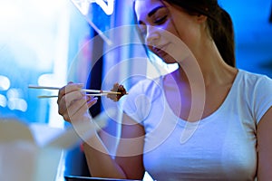 Close up of attractive woman eating asian food with chopsticks at restaurant.