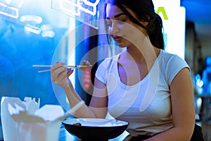 Close up of attractive woman eating asian food with chopsticks at restaurant.