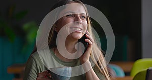 Close up of attractive woman with long hair drinking coffe and speaking on phone happily in cafe