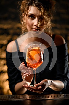 Close-up of attractive young woman at bar holds in her hand glass with cocktail