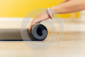 Close-up of an attractive young woman folding a black yoga or fitness mat after a workout. Healthy lifestyle, keep fit