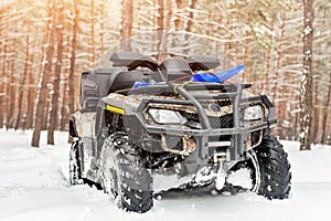 Close-up ATV 4wd quad bike in forest at winter. 4wd all-terreain vehicle stand in heavy snow with deep wheel track. Seasonal