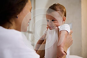 Close-up authentic portrait of an adorable baby boy smiling to his mother holding him in arms. Babyhood and Infancy time