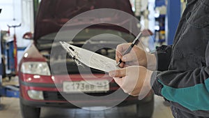 Close Up of Auto Mechanics a Writing on a Clipboard in Garage. Auto Service