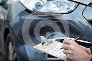 Close Up Of Auto Workshop Mechanic Inspecting Damage To Car And Filling In Repair Estimate