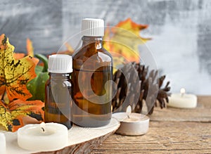 Close up autumn spa concept with essential oil bottle, dried leaves, burning candles on wooden background.