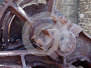 Close up of an axle and broken spoked wheel on old rusted abandoned industrial machinery against a stone wall photo