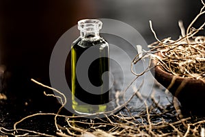 Close up of ayruvdic essence of khus or vetiver grass in a small bottle with raw dried khus in a clay bowl on wooden surface.