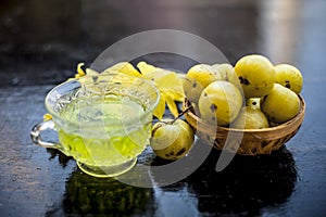 Close up of ayurvedic and organic tea of amla or Indian gooseberry in a transparent cup on wooden surface with raw amla in a fruit