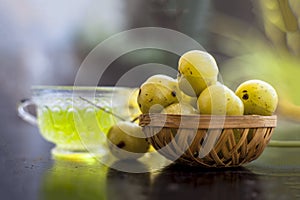 Close up of ayurvedic and organic tea of amla or Indian gooseberry in a transparent cup on wooden surface with raw amla in a fruit