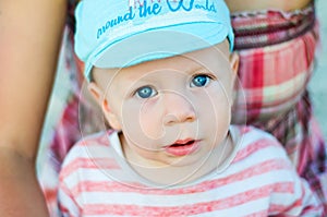 Close up of baby boy face with blue eyes with open mouth and blue cap. Child and children emotions