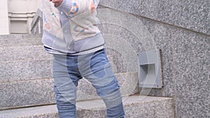 Close up of a baby boy feets in blue sneakers and jeans going down the granite ladder step by step in the city park on