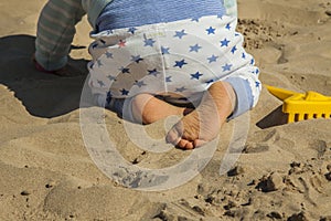 Close up baby boy playing with sand toys at the beach. Rear view