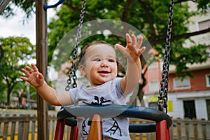 Close up of baby girl playing on outdoor playground swing. Toddler playing on school or kindergarten yard. Active kid on colorful