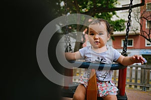 Close up of baby girl playing on outdoor playground swing. Toddler playing on school or kindergarten yard. Active kid on colorful