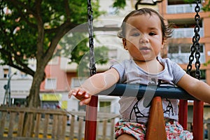 Close up of baby girl playing on outdoor playground swing. Toddler playing on school or kindergarten yard. Active kid on colorful