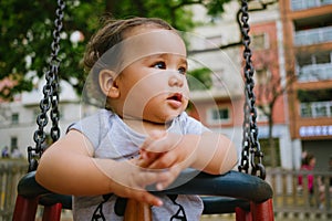 Close up of baby girl playing on outdoor playground swing. Toddler playing on school or kindergarten yard. Active kid on colorful