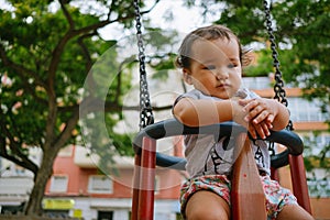 Close up of baby girl playing on outdoor playground swing. Toddler playing on school or kindergarten yard. Active kid on colorful