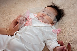 Close-up of a baby girl who was just born recently. on a soft brown bed There was a mother`s hand holding her hand to keep her