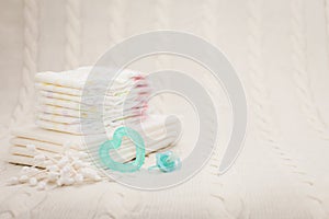 Close up baby hygiene items. stack of diapers, ear sticks, baby dummy and teether in selective focus