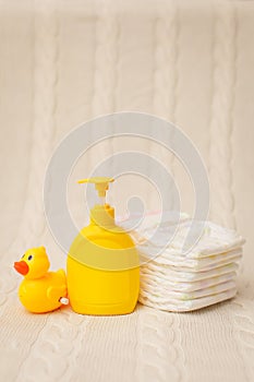 Close up baby hygiene items. stack of diapers, liquid soap and yellow duck on beige plaid in selective focus