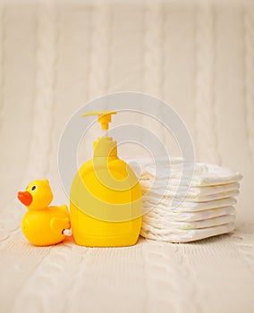 Close up baby hygiene items. stack of diapers, liquid soap and yellow duck on beige plaid in selective focus