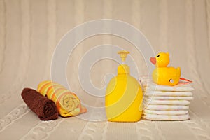 Close up baby hygiene items. stack of diapers, liquid soap and yellow duck on beige plaid in selective focus