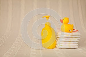 Close up baby hygiene items. stack of diapers, liquid soap and yellow duck on beige plaid in selective focus