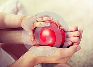 Close up of baby and mother hands with red heart