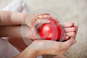 Close up of baby and mother hands with red heart