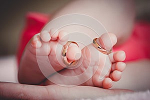 Close up of baby`s feet with wedding rings in mother`s hands. Newborn. Selective focus