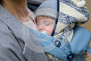 Close up of a baby sleeping in a baby carrier on his mother's chest or cleavage, in an exceptionally intimate closeness photo