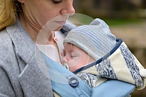 Close up of a baby sleeping in a baby carrier on his mother's chest or cleavage, in an exceptionally intimate closeness photo