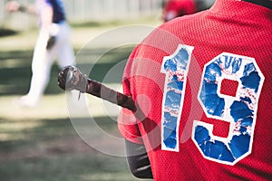 Close-up of the back of a baseball player holding a bat with the number 19 on a red shirt