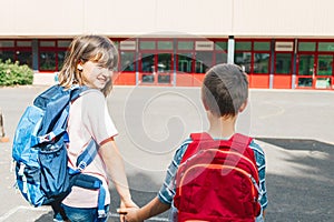 Close-up from the back of a brother and sister with backpacks on their backs going to school. The girl turned around and
