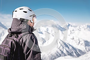 Close-up back view athlete skier in helmet and ski mask against the snow-capped mountains of a ski resort with a