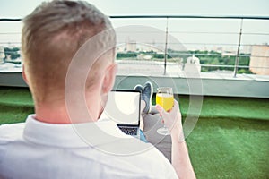 Close up back view businessman with drink comfortably working on laptop with white blank screen sitting on terrace with Urban Land