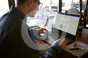 Close-up back view of caucasian businessman hands typing on laptop keyboard and using touchpad. Notebook and pen on