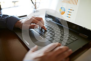 Close-up back view of caucasian businessman hands typing on laptop keyboard and using touchpad. Notebook and pen on