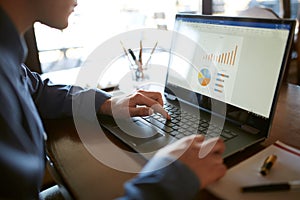 Close-up back view of caucasian businessman hands typing on laptop keyboard and using touchpad. Notebook and pen on