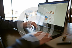 Close-up back view of caucasian businessman hands typing on laptop keyboard and using touchpad. Notebook and pen on